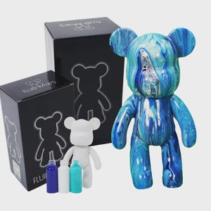 Peut inclure: Une figurine d'ours marbrée bleu et blanc avec une figurine d'ours blanche vierge et des flacons de peinture. Les figurines d'ours sont sur une surface blanche. Les boîtes sont noires avec du texte blanc qui dit "Fluid Paws".