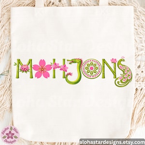 May include: White tote bag with the word "MAHJONGS" in green bamboo-style letters. The letters are decorated with pink flowers, a green dragon, and a peacock. The shop's name and website are at the bottom.