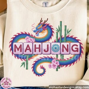 May include: Cream-colored sweatshirt featuring a colorful dragon design with the word "MAHJONG" in a block letter style. The dragon is blue, purple, and yellow, with pink flowers and bamboo stalks. The Etsy shop URL is visible at the bottom.