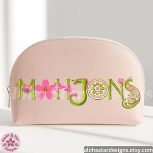May include: A light pink cosmetic bag with a zipper closure. The word "MAHJONG" is displayed across the front in a decorative font with floral and dragon accents. The bag has a rounded shape and a smooth texture.
