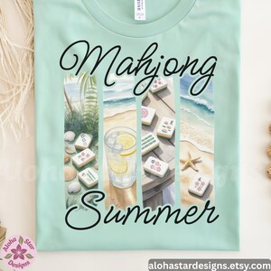 May include: A pale green t-shirt with the words "Mahjong Summer" in a script font. The design features watercolour images of mahjong tiles, a drink with lemon, and a beach scene. The shirt has a crew neck.