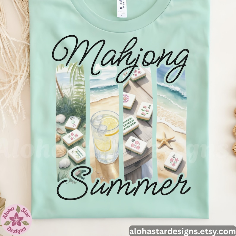 May include: A pale green t-shirt with the words "Mahjong Summer" in a script font. The design features watercolour images of mahjong tiles, a drink with lemon, and a beach scene. The shirt has a crew neck.