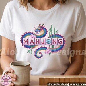 May include: White t-shirt featuring a colorful dragon design with the word "MAHJONG" in a decorative font. The design includes bamboo stalks and pink flowers. The Etsy shop URL is visible at the bottom.
