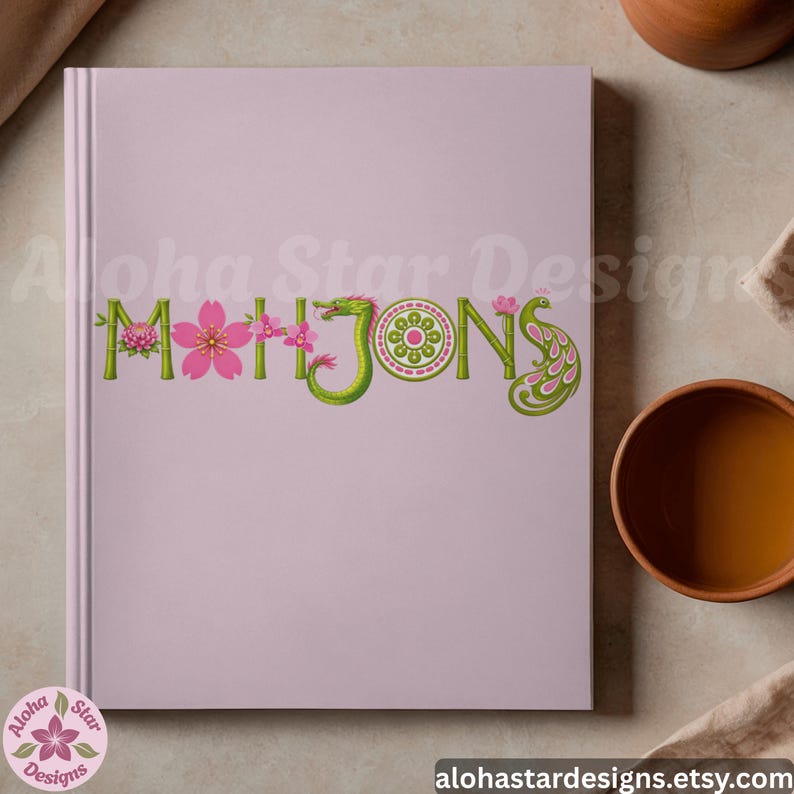 May include: A light pink journal with the word "MAHJONG" embroidered across the front in green, pink, and white. The letters are decorated with flowers and a dragon. The journal has a spiral binding and the shop's logo in the bottom left corner.