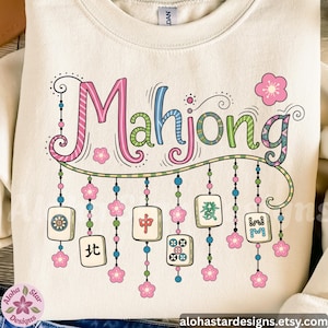 May include: Cream-colored sweatshirt with the word "Mahjong" in colorful, whimsical lettering. The design includes hanging tiles, pink flowers, and decorative beads, evoking a playful, game-themed aesthetic.
