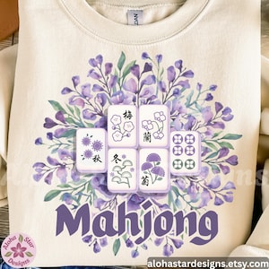 May include: Cream-colored sweatshirt featuring a purple floral design and Mahjong tiles. The design includes the word "Mahjong" in purple script. The tiles are surrounded by a watercolor floral arrangement in shades of purple and green.