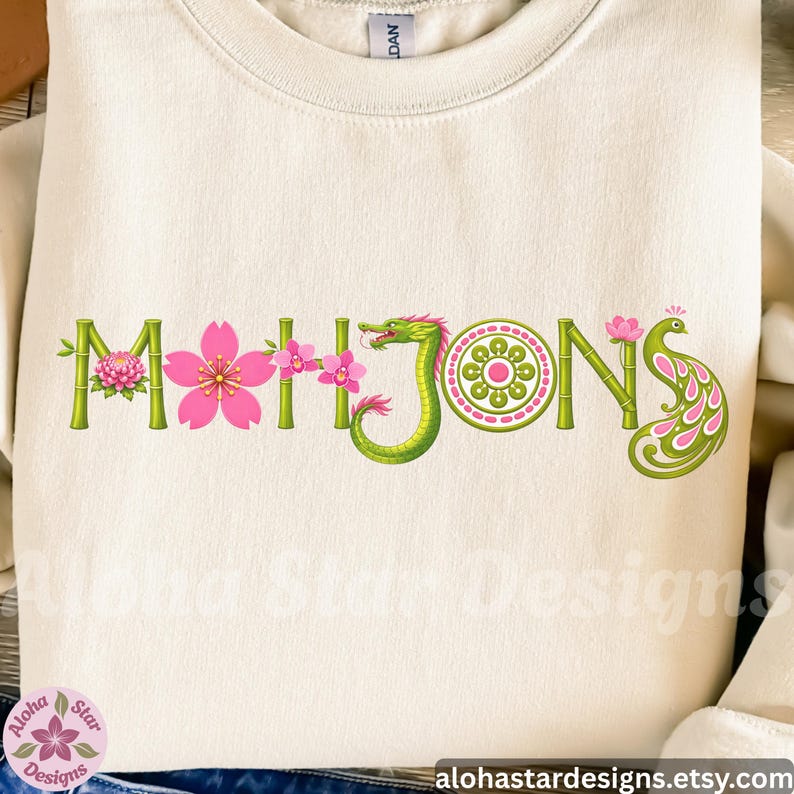 May include: Cream-colored sweatshirt with the word "Mahjong" in a decorative design. The letters are green bamboo with pink flowers and a green dragon. The letter "O" is a green circle with a pink flower design, and the letter "S" is a pink and green peacock.