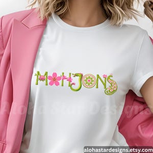 May include: White t-shirt with the word "MAHJONG" in green, pink, and white embroidery. The design incorporates cherry blossoms, a dragon, and a peacock feather. The Etsy shop URL is visible at the bottom.