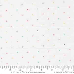 May include: White fabric with a repeating pattern of small, colorful crosses in shades of red, yellow, teal, and gray. The crosses are evenly spaced across the fabric's surface. A ruler is visible along the bottom edge.