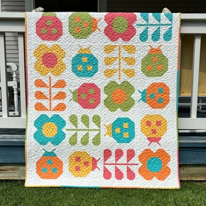 May include: A quilt featuring a repeating grid pattern of ladybugs, flowers, and leafy stems. The design uses a white background with a leaf-patterned texture and colorful fabric blocks in shades of pink, orange, yellow, green, and teal blue.