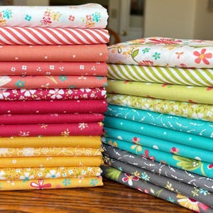 May include: Stacks of colorful fabric in various floral and striped patterns. The fabrics are in shades of pink, yellow, green, and blue. The fabric is likely cotton and suitable for quilting or other craft projects.
