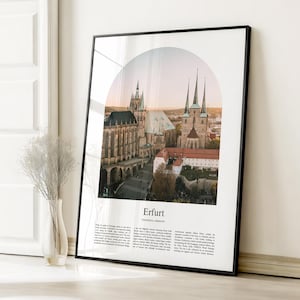 May include: Framed print featuring a scenic view of Erfurt, Germany, showcasing historic architecture under a soft, sunset-colored sky. The print includes the city's name in a clean, modern font, and is encased in a sleek black frame.