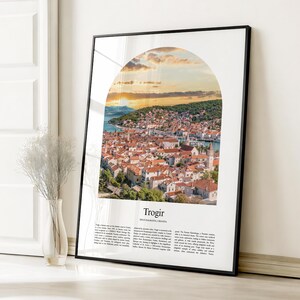 Könnte beinhalten: Ein gerahmter Druck mit einer malerischen Ansicht von Trogir, Kroatien, unter einem Sonnenuntergangshimmel. Das Bild ist in einer Bogenform angeordnet und zeigt die roten Ziegeldächer und die Küstenlandschaft der Stadt. Der Druck enthält das Wort "Trogir" und beschreibenden Text.
