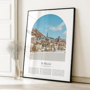 Puede incluir: Un póster enmarcado con una vista panorámica de St. Moritz, Suiza, bajo un cielo azul. La imagen, en forma de arco, muestra un paisaje nevado con edificios y un campanario. La impresión está en un marco negro.