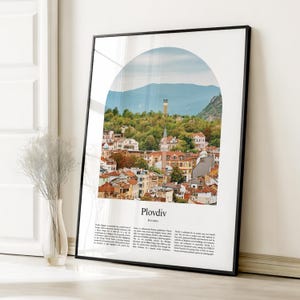 May include: Framed art print featuring a scenic view of Plovdiv, Bulgaria, under an arched window. The image showcases a cityscape with red-tiled roofs, a tall tower, and a backdrop of green hills and a blue sky. The word "Plovdiv" is displayed.