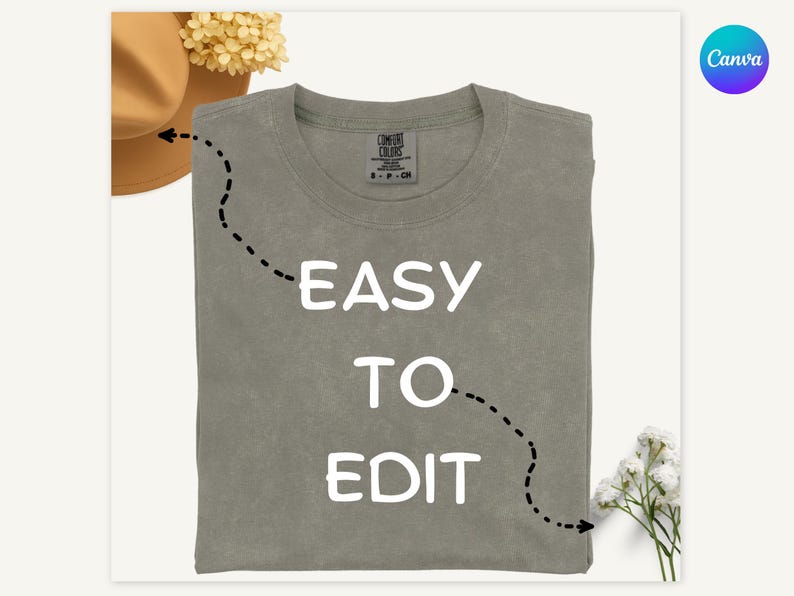 May include: A sage green t-shirt with the words "EASY TO EDIT" in white block letters. The shirt is folded and has a tag on the collar. A brown hat and flowers are in the background.