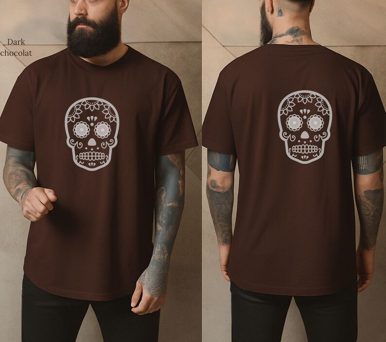 May include: Dark chocolate brown t-shirt featuring a white sugar skull design on the front and back. The skull has floral and dot details. The shirt is a short-sleeved crew neck.
