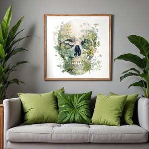 May include: A framed watercolor print of a skull adorned with flowers and greenery. The artwork features a light-colored skull with dark eye sockets and a black nose cavity. The skull is surrounded by daisies and other foliage, set against a white background.