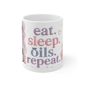Könnte beinhalten: Ein weißer Keramikbecher mit dem Text eat. sleep. oils. repeat. in violetten, rosafarbenen und blauen Farbverlauf-Buchstaben. Das Design enthält aquarellartige violette und rosa Akzente, kleine Herzumrisse und eine kleine braune Ölflasche.