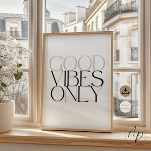 May include: A framed print with the words "GOOD VIBES ONLY" in a stylish font. The words "GOOD" and "ONLY" are in black, while "VIBES" is in a light brown color. The print is displayed on a windowsill with a view of a European-style building.