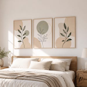 Könnte beinhalten: Drei gerahmte botanische Kunstdrucke. Jeder Druck zeigt ein minimalistisches Design mit einem dunkelgrünen Blattzweig vor einem Hintergrund aus beige- und olivgrünen Formen. Die Rahmen sind hellholzfarben.