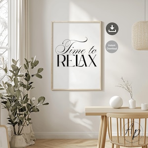 Könnte beinhalten: Ein gerahmter Druck mit den Worten "Time to RELAX" in schwarzer Schrift und Blockbuchstaben. Der Druck befindet sich in einem hellen Holzrahmen und hängt an einer weißen Wand. Der Raum ist mit einer Pflanze, einem Tisch und einer gewebten Leuchte dekoriert.