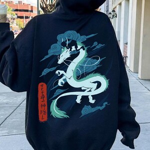 May include: Black hoodie featuring a white and teal dragon design with cloud accents. The dragon is the focal point, with Japanese text on the lower left. The hoodie has a drawstring hood and long sleeves.