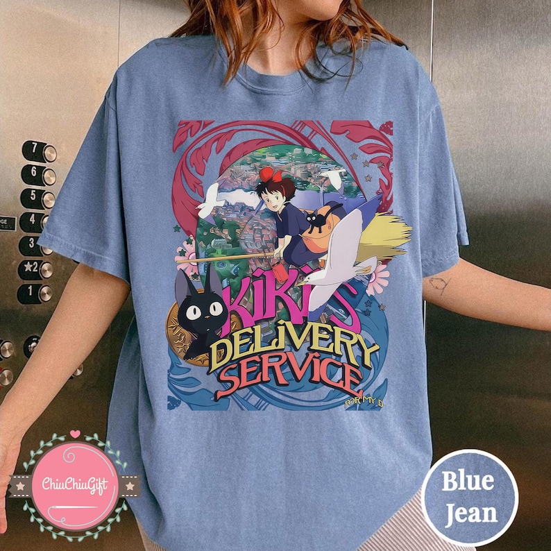 May include: Pale blue t-shirt with a vibrant graphic from "Kiki's Delivery Service." The design shows Kiki on a broom, a black cat, and the words "Kiki's Delivery Service."