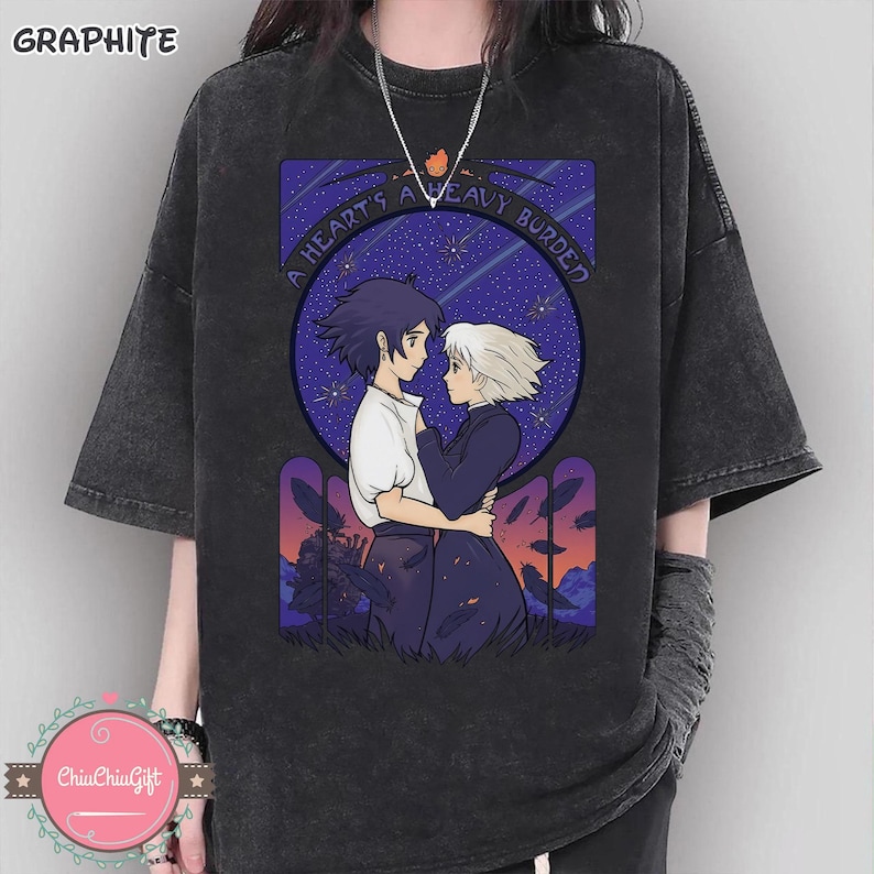 Puede incluir: Camiseta de color grafito con una ilustraci&oacute;n de estilo anime que muestra a dos figuras abraz&aacute;ndose bajo un cielo estrellado. El dise&ntilde;o incluye el texto "A HEART'S A HEAVY BURDEN" en un marco circular. La camiseta tiene mangas cortas y un corte holgado.