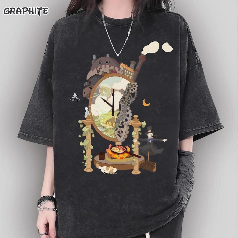 Op de afbeelding: Graphietkleurig, oversized T-shirt met een grillig klokontwerp met tandwielen, een huis en een kok. Het ontwerp bevat een wijzerplaat, een schoorsteen en een klein figuur. Het shirt heeft korte mouwen.