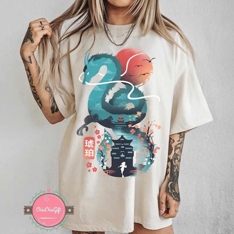 Puede incluir: Camiseta color crema con un dise&ntilde;o de drag&oacute;n turquesa, un sol rojo y texto japon&eacute;s. El drag&oacute;n envuelve un paisaje con una pagoda, flores de cerezo y una figura. La camiseta tiene un corte holgado.