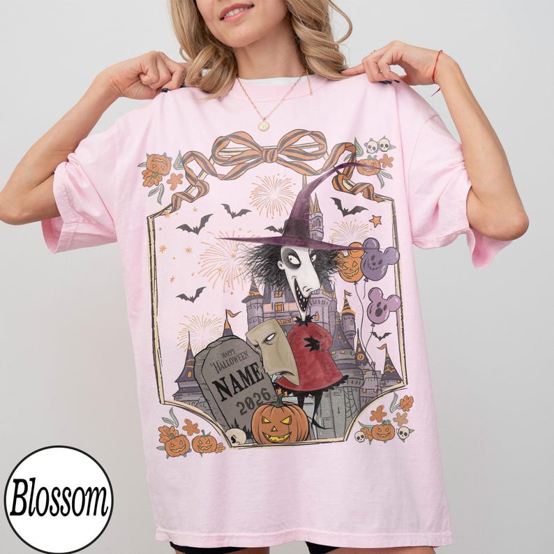 Pode incluir: Uma t-shirt rosa claro com uma estampa gr&aacute;fica de um personagem alto e magro com um chap&eacute;u de bruxa ao lado de uma l&aacute;pide com a inscri&ccedil;&atilde;o "Happy Halloween NAME 2026". O design inclui um castelo, morcegos, fogos de artif&iacute;cio, ab&oacute;boras e bal&otilde;es.