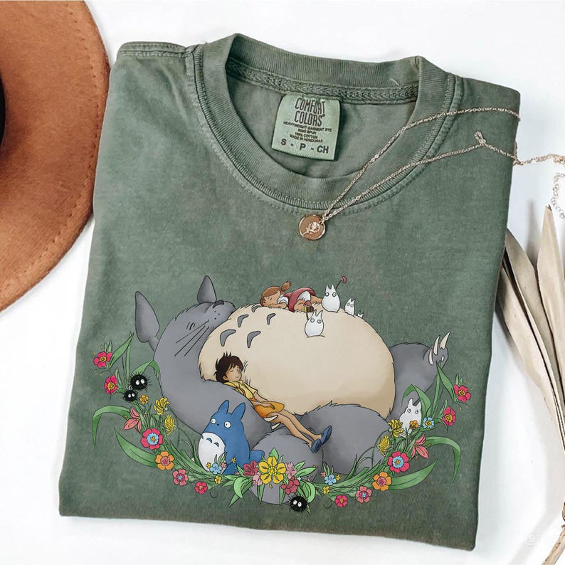 Puede incluir: Camiseta verde Comfort Colors con un gr&aacute;fico de Totoro de Mi Vecino Totoro, rodeado por una corona floral. La camiseta tiene el logo de Comfort Colors y un peque&ntilde;o collar con colgante. La camiseta es talla S-P-CH.
