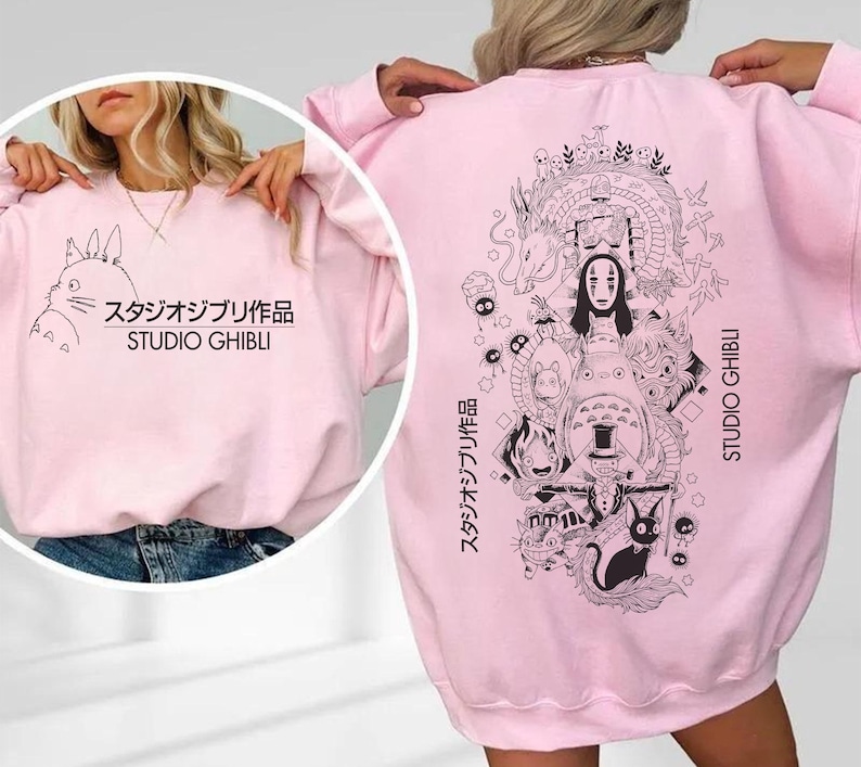 May include: A light pink Studio Ghibli sweatshirt. The front features a Totoro graphic and Japanese text. The back displays a detailed black and white illustration of characters from Studio Ghibli films, with the words "Studio Ghibli" in English and Japanese.