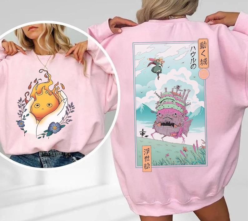 K&ouml;nnte beinhalten: Hellrosa Sweatshirt mit einem Grafik eines Feuergeistes in einer Hand auf der Vorderseite. Die R&uuml;ckseite zeigt eine japanische Anime-Szene mit einer Burg, einer Figur und Text. Das Sweatshirt ist aus weichem Material.