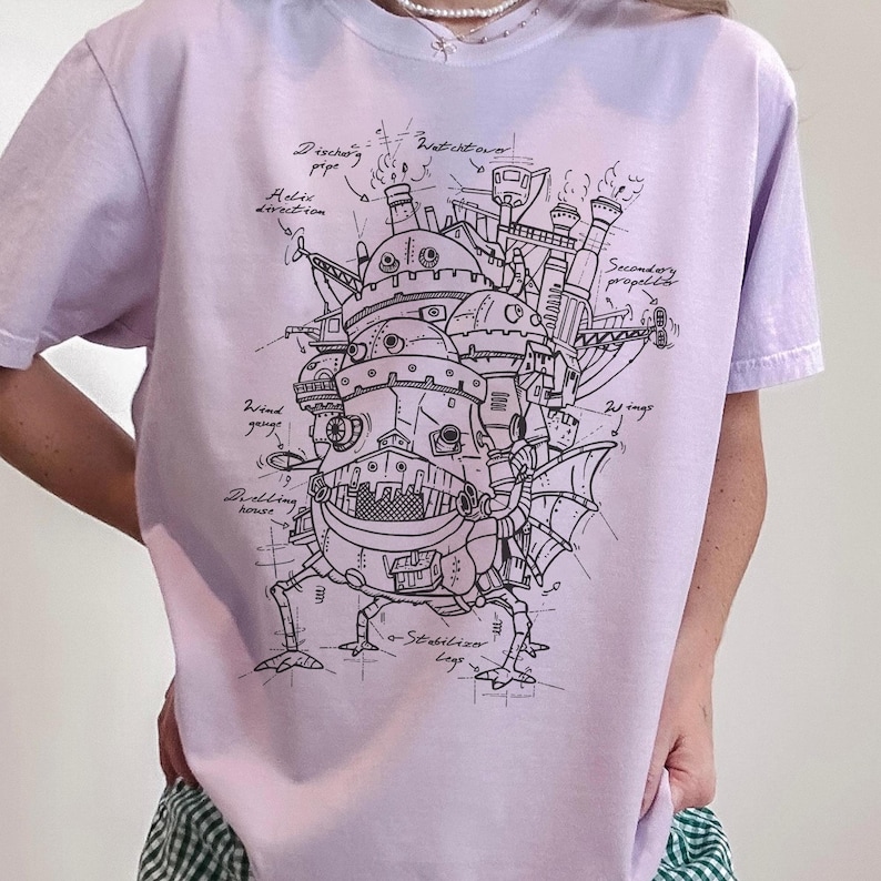 May include: A light purple t-shirt featuring a detailed black and white illustration of a mechanical structure with various labeled components. The design includes text such as "Discharge pipe" and "Wind gauge".
