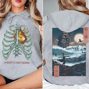 May include: Gray hoodie featuring a cartoon heart inside a rib cage with the text "A Heart's A Heavy Burden" on the front. The back of the hoodie has a colorful illustration with Japanese text.