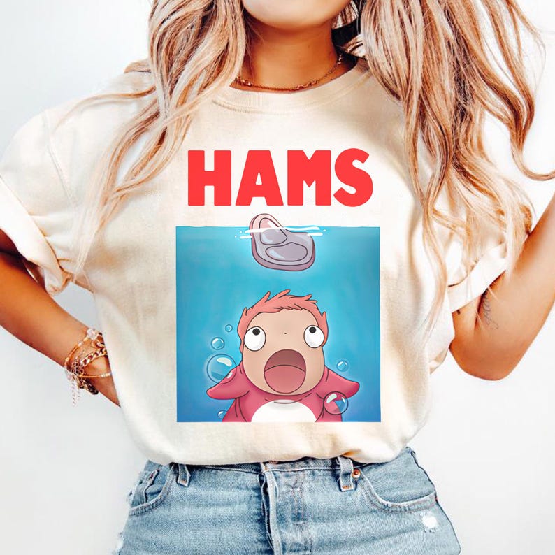 May include: Cream-coloured t-shirt with the word "HAMS" in red block letters. Below is a cartoon illustration of a pink character and a piece of meat in water with bubbles.