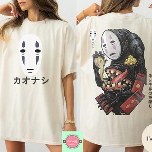 May include: Ivory-colored t-shirt featuring a white mask design with black details and Japanese text. The back of the shirt displays a black creature with a white mask, a long tongue, and Japanese text.