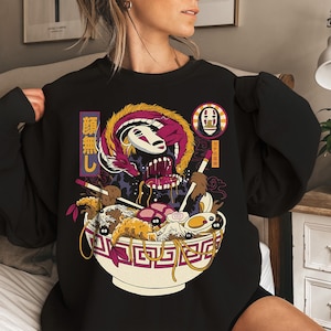 K&ouml;nnte beinhalten: Schwarzes Sweatshirt mit einer farbenfrohen Anime-Illustration einer Ramen-Sch&uuml;ssel, eines Drachen und einer Figur mit wei&szlig;er Maske. Die Sch&uuml;ssel enth&auml;lt Nudeln, Eier und andere Zutaten. Japanischer Text ist sichtbar.