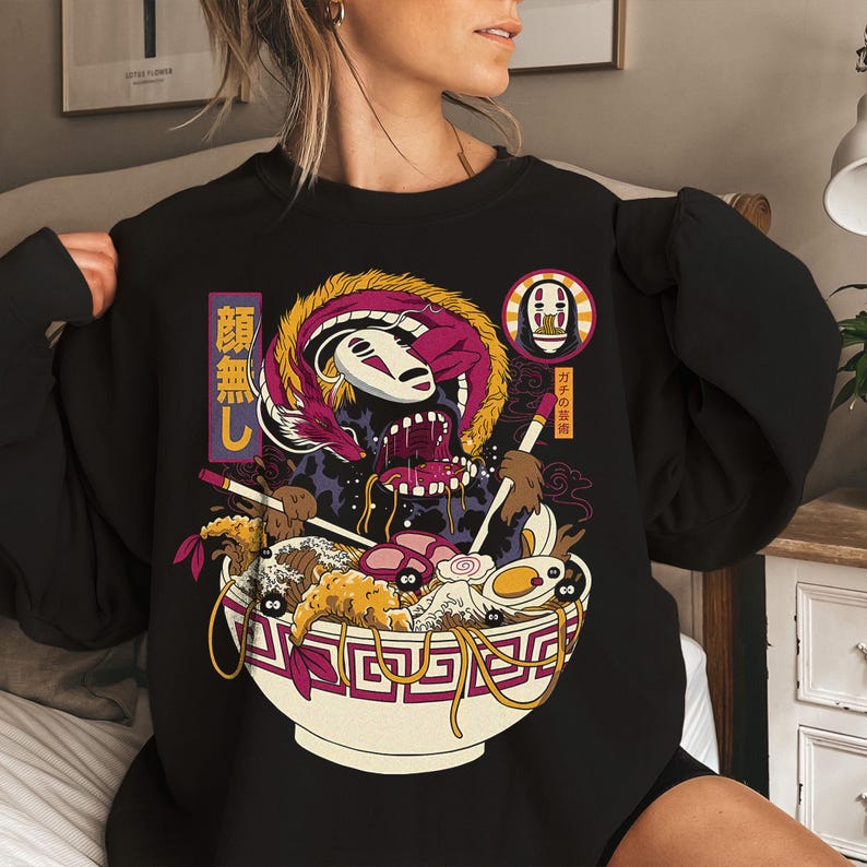 K&ouml;nnte beinhalten: Schwarzes Sweatshirt mit einer farbenfrohen Anime-Illustration einer Ramen-Sch&uuml;ssel, eines Drachen und einer Figur mit wei&szlig;er Maske. Die Sch&uuml;ssel enth&auml;lt Nudeln, Eier und andere Zutaten. Japanischer Text ist sichtbar.