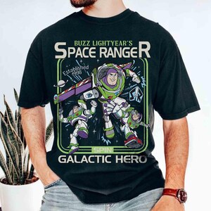 May include: Black t-shirt with a Buzz Lightyear graphic. The design features Buzz in his space ranger suit, the text "Buzz Lightyear's Space Ranger", and "Galactic Hero". Established 1998.