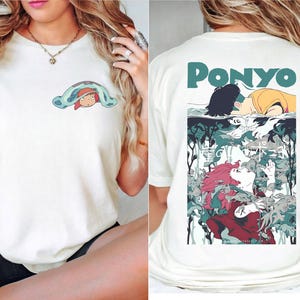May include: Off-white t-shirt featuring a cartoon illustration. The front displays a character under a blue blanket. The back has the word "PONYO" above a colorful anime-style graphic with characters and aquatic elements.