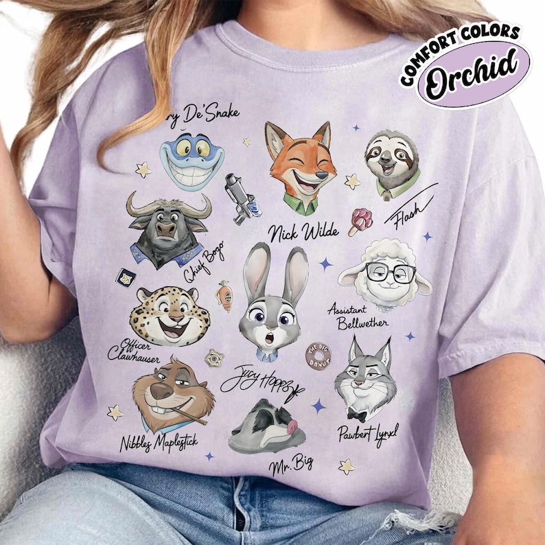 Op de afbeelding: Een lichtpaars T-shirt met stripfiguren uit Zootopia. Het shirt bevat personages als Nick Wilde, Judy Hopps en Flash, met de tekst "COMFORT COLORS Orchid".