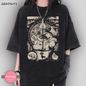Puede incluir: Camiseta negra con estampado gr&aacute;fico que presenta el texto "PRINCESS MONONOKE IN THE FOREST" y una ilustraci&oacute;n de una mujer, un lobo y animales del bosque. La camiseta tiene mangas cortas y un corte holgado. La palabra "GRAPHITE" est&aacute; impresa arriba a la izquierda.