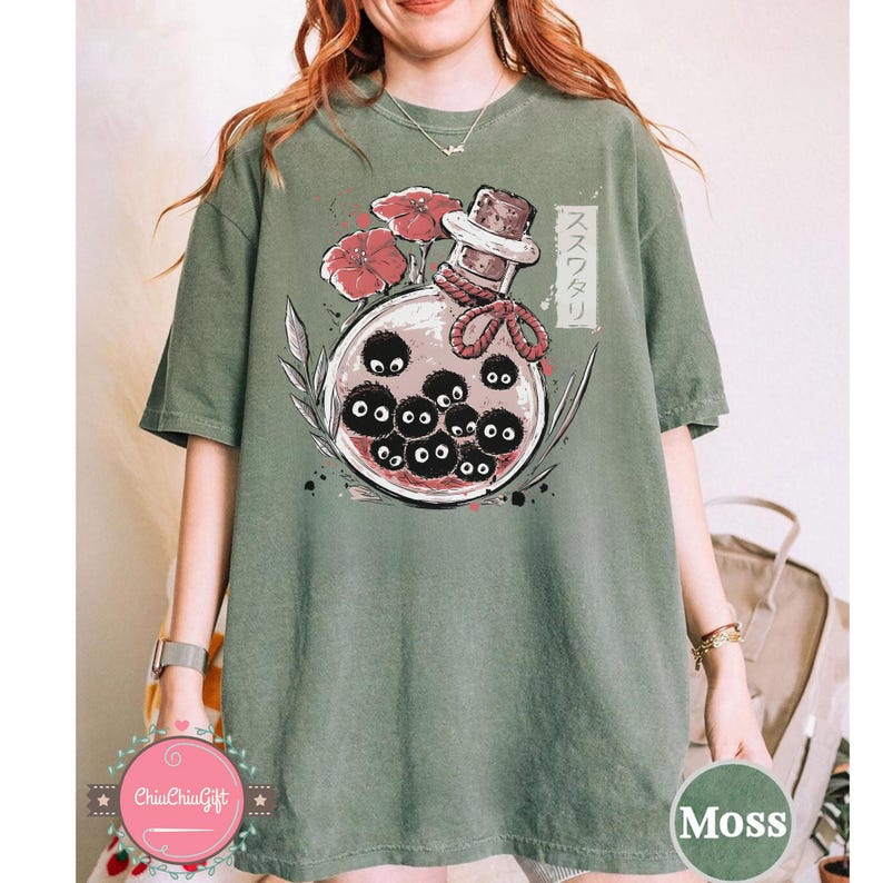 Puede incluir: Camiseta verde musgo con un gr&aacute;fico de una botella de vidrio con sprites de holl&iacute;n negros y flores rojas. Texto japon&eacute;s en el lado derecho. La camiseta tiene un tap&oacute;n de corcho.
