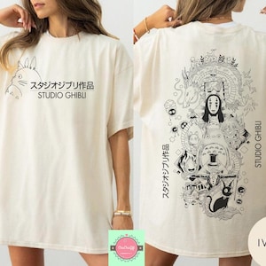May include: Ivory-colored t-shirt featuring a Studio Ghibli design. The front displays a Totoro graphic with Japanese text and "STUDIO GHIBLI." The back showcases a detailed black and white illustration of various characters and the text "STUDIO GHIBLI."