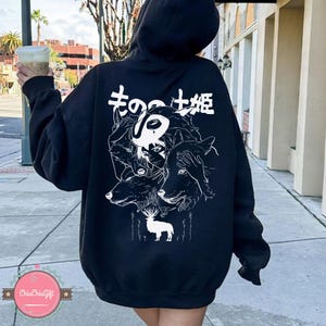 May include: Black hooded sweatshirt with a white graphic on the back featuring a stylized illustration of a person, wolves, and a deer, with Japanese text at the top. The sweatshirt has a drawstring hood.