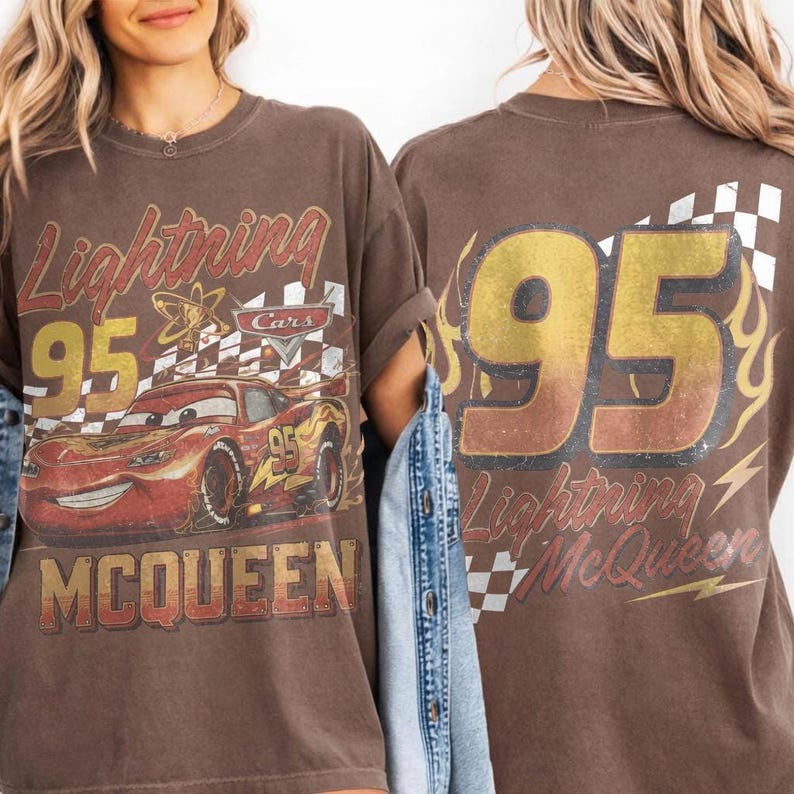 May include: A brown t-shirt featuring a graphic of the red race car Lightning McQueen with the number 95, a checkered flag pattern, and the text Lightning McQueen. The back of the shirt displays a large number 95 with flames and a checkered pattern.