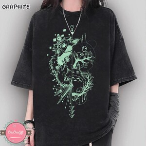 Puede incluir: Camiseta de color grafito con un dise&ntilde;o gr&aacute;fico &uacute;nico. El dise&ntilde;o presenta una imagen dividida con un esp&iacute;ritu del bosque y otros personajes en color verde claro. La camiseta tiene mangas cortas y un corte relajado.